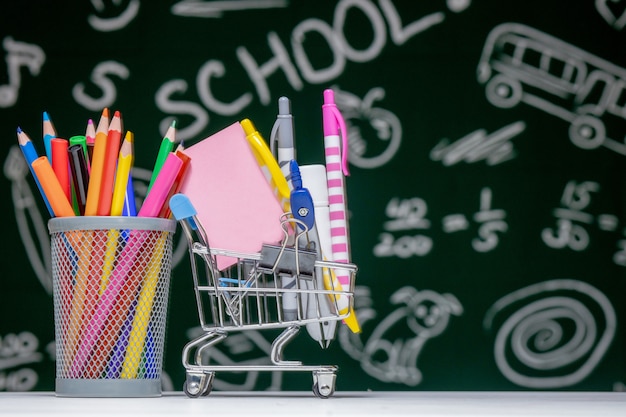 Back to school background with books, pencils and globe on white table on a green blackboard background.