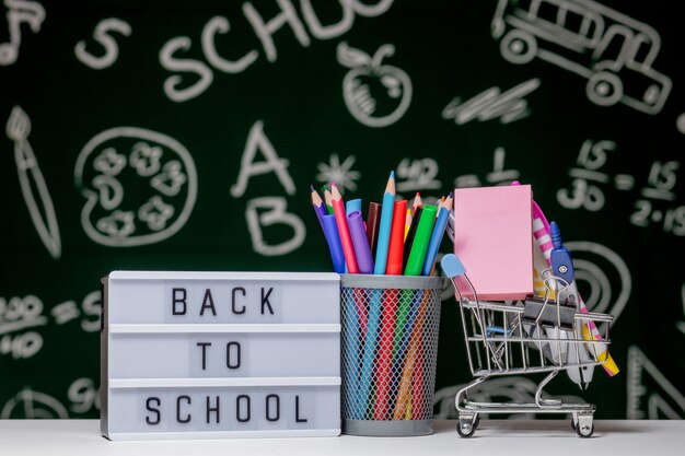 Foto di nuovo al fondo della scuola con i libri, le matite e il globo sulla tavola bianca su un fondo verde della lavagna.