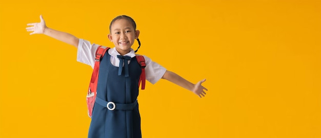 학교 배너 아이디어 개념으로 돌아가서 제복을 입은 행복한 아시아 여고생은 디자인 작업을 위한 클리핑 패스를 사용하여 노란색 배경에 격리된 손 기쁨과 영감을 퍼뜨리며 빈 여유 공간을 만듭니다.