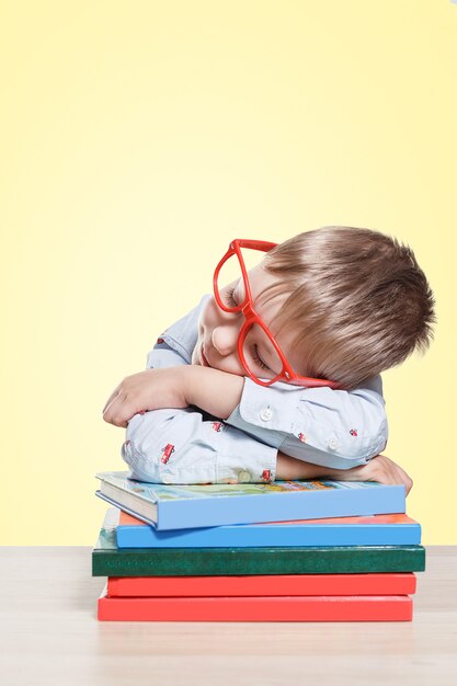 Back to school. Child boy in red glasses sitting at desk and sleeping on the books. Pupil of primary school.