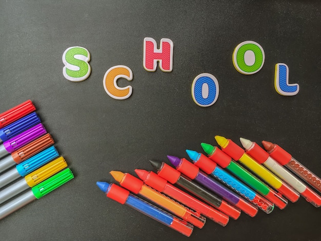 Photo back to school concept. colored pencils on black background with the word school .