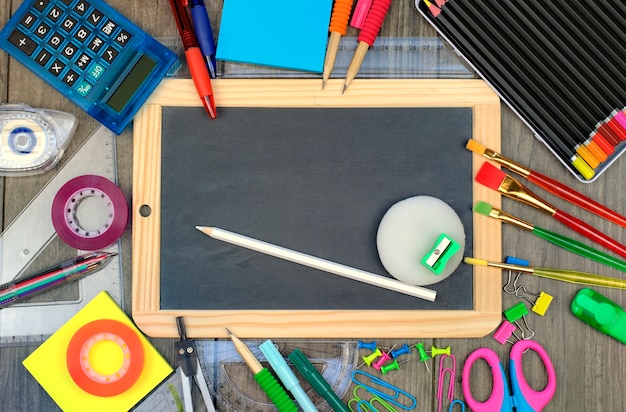 Di nuovo al concetto della scuola: rifornimenti di scuola e dell'ufficio con una lavagna su un fondo di legno