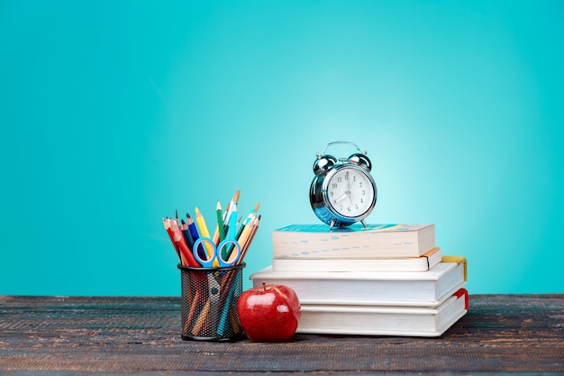 Back to School concept.School Books, colored pencils and clock on blue wall