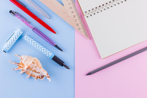 Back to school concept School stationery and seashell on pink blue background Pens pencil and gon