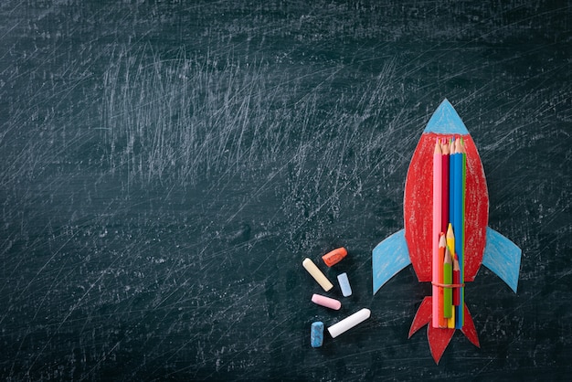 Back to school Concept. Top view of Painted paper rocket on chalkboard.