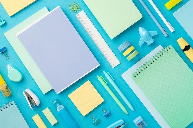 Back to school concept Top view photo of colorful copybooks plane shaped sharpener adhesive tape binder clips marker pens erasers ruler stapler paper sticky notes correctors isolated blue background