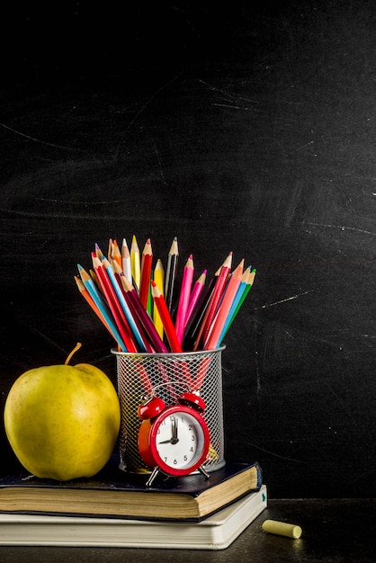 Back to school concept with books alarm clock color pencils chalkboard background