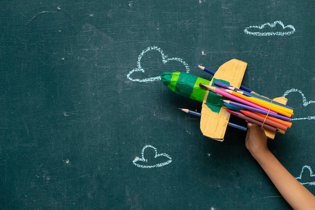 Back to school concept with Paper rocket made from pencils over chalkboard backgroundxAThe hand of the child is holding Paper rocket