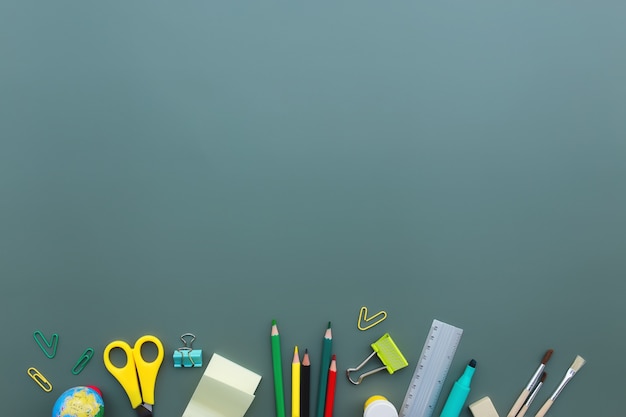 Back to school conceptual flat lay with different office supply objects on green background. Concept for primary and secondary school pupil. Scissors, pen, pencil, eraser, ruler, note, clip