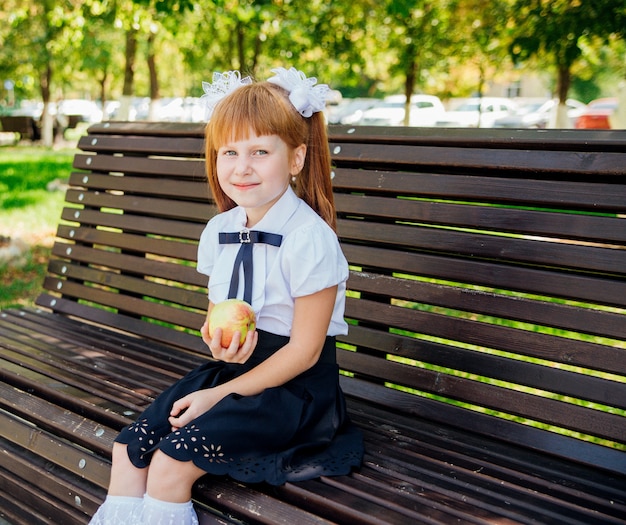 学校に戻る。かわいい小さな女子高生が校庭のベンチに座って、青リンゴを持っています。