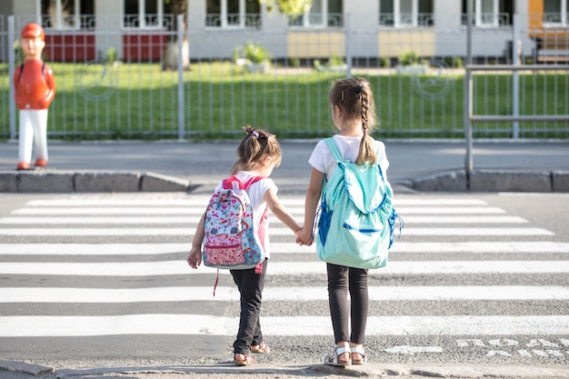 Back to school education concept with girl kids, elementary students, carrying backpacks going to class