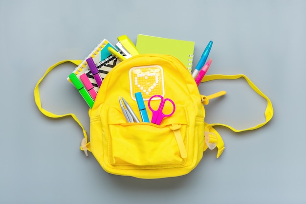 Back to school, education concept. yellow backpack with school supplies - notebook, pens, ruler, calculator, scissors isolated on gray surface. top view