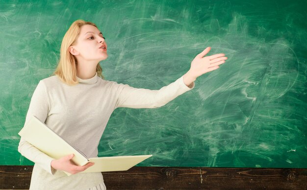 Back to school. Education. School. Job. Teacher in classroom. Teacher with folder. Female teacher with folder near chalkboard. Teacher with classroom journal talks with students.