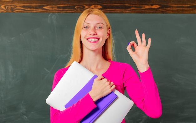 Back to school. Education. Smiling female teacher in classroom shows Sign ok. University. College.