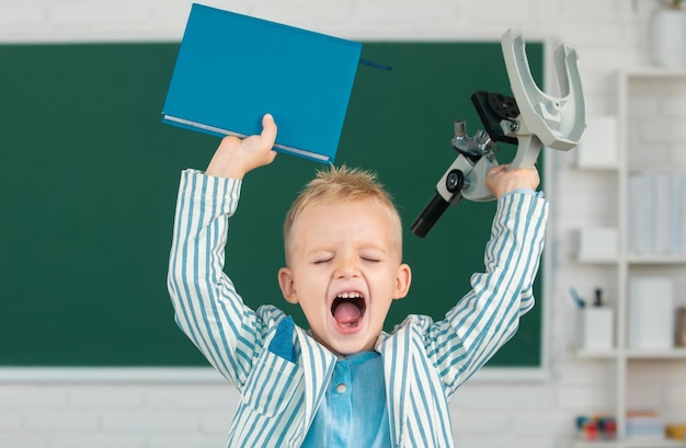 Back to school excited schoolboy pupil with microscope and book funny face of little student of