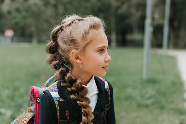 Ritorno a scuola faccia ritratto piccolo bambino felice allievo studentessa otto anni in uniforme di moda con zaino e acconciatura voluminosa lunga treccia pronta per andare secondo grado primo giorno di scuola primaria