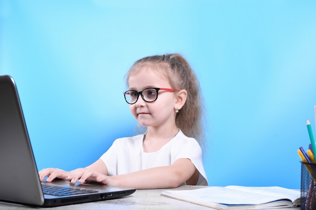 다시 학교로. 행복하고 귀여운 부지런한 아이가 실내 책상에 앉아 있습니다. 아이는 노트북, 컴퓨터와 가정에서 수업 시간에 학습