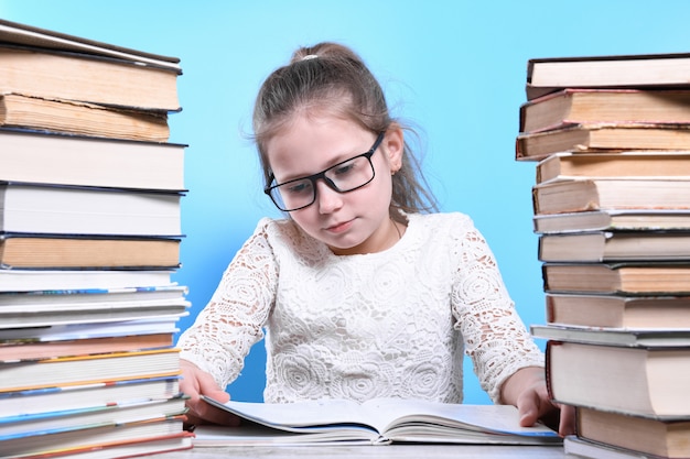 Back to school .Happy cute industrious child is sitting at a desk indoors. Kid is learning in class.Mountains of books on the sides