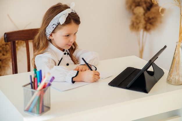 Back to school Happy little schoolgirl sitting at her Desk The girl does her homework using a tablet computer online education