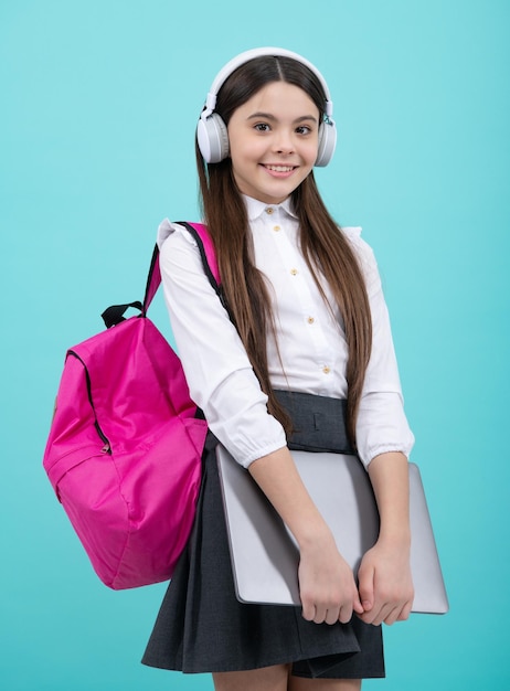 Back to school Happy teenager school girl in school uniform with bagpack headphones and laptop School children on isolated blue background