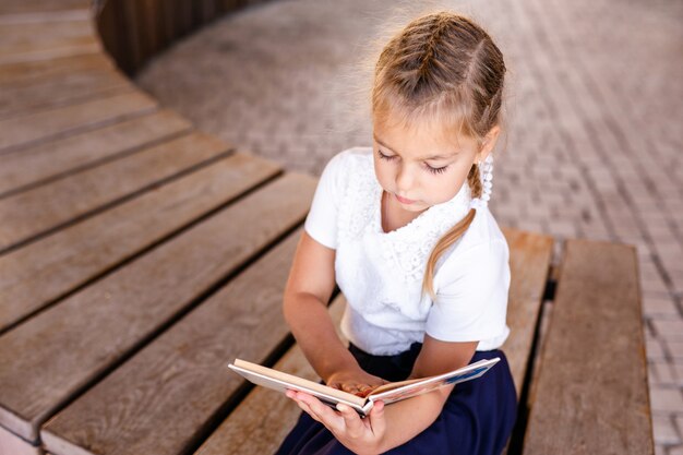 Ritorno a scuola e tempo felice carino bambino industrioso seduto all'aperto. ragazza che legge il libro.