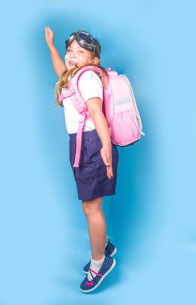 Ritorno a scuola, ispirazione per l'apprendimento dei bambini nell'educazione scientifica, ricerca della conoscenza. carina studentessa delle elementari in uniforme blu bianca, con occhiali volanti, che salta su uno sfondo blu colorato