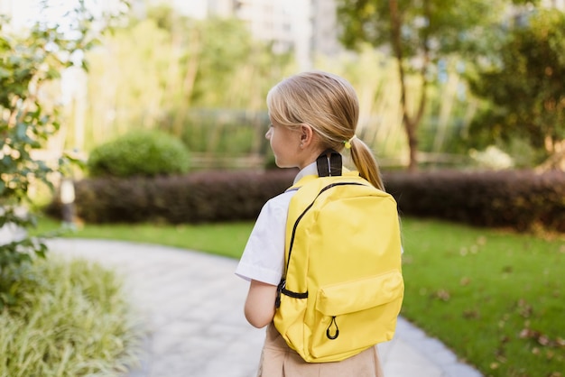 Back to school little girl with yellow backpack from elementary school outdoor