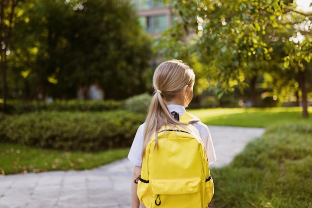 Back to school little girl with yellow backpack from elementary school outdoor