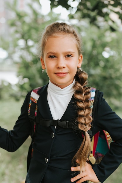 Back to school little happy kid pupil schoolgirl eight years old in fashion uniform with backpack and hairstyle voluminous long braid ready going to second grade first day at primary school