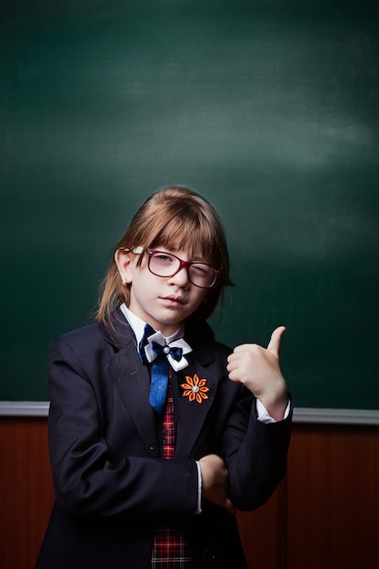 Back to school. love to learning. Thumb up. The girl in uniform and glasses smiles, gestures to the side