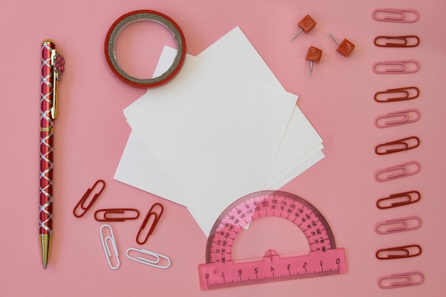 Back to school . Paper for writing with pencils, clips and tape on a pink background.