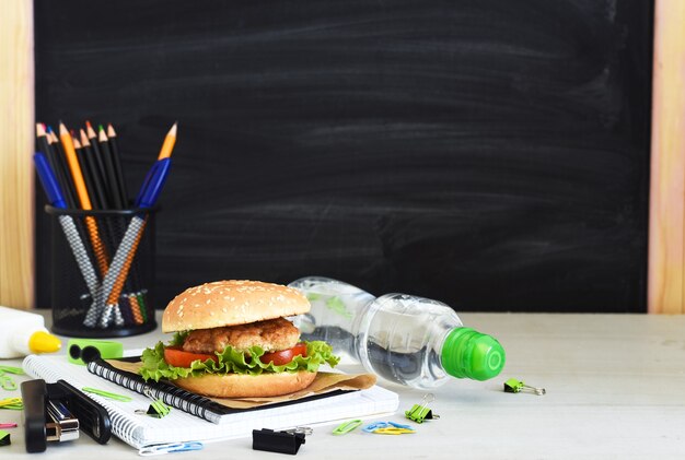 Di nuovo a scuola. educazione in quarantena. pranzo al sacco con hamburger, acqua e accessori per la scuola sullo sfondo del consiglio scolastico.