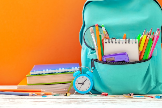 Back to School. School Backpack with different supplies and alarm clock on orange background