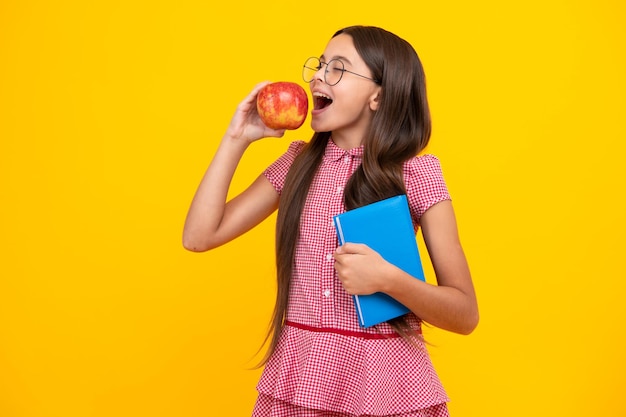 Back to school School child teenage student girl with bagpack hold apple and book isolated on yellow Amazed teen girl Excited expression cheerful and glad