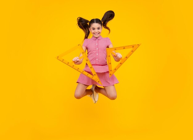 Back to school School girl hold ruler measuring isolated on yellow background Crazy jump jumping kids Happy teenager positive and smiling emotions of teen schoolgirl