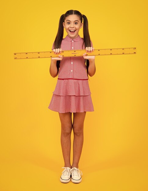 Back to school school girl hold ruler measuring isolated on yellow background happy teenager positive and smiling emotions of teen schoolgirl