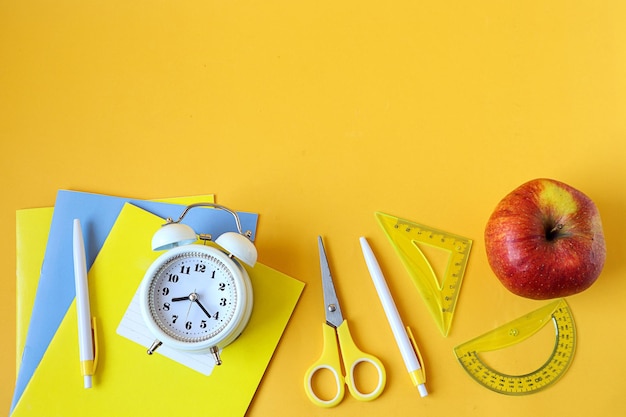 Back to school school supplies red apple alarm clock on yellow background space for text top view