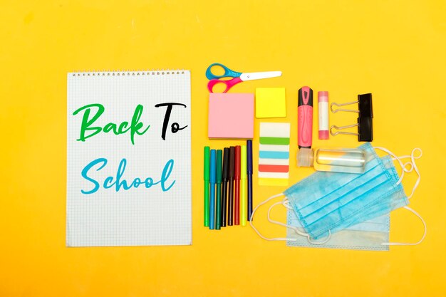 Photo back to school school supplies with medical face mask and empty notebook on a yellow background