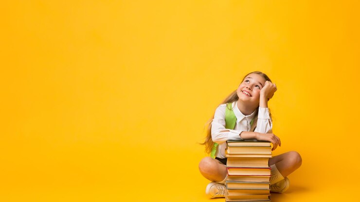 Photo back to school schoolgirl dreaming sitting with backpack at books stack posing over yellow studio