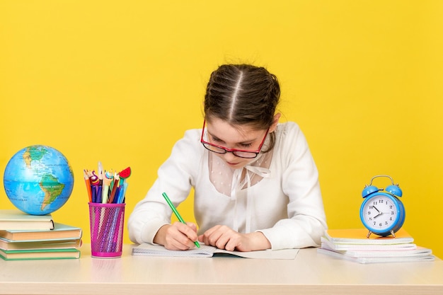 Back to school The schoolgirl sits at the desk and thinks about the decision of the task on yellow background