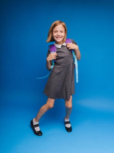 Back to school A schoolgirl with a school bag on an isolated blue studio background a little girl is holding a backpack