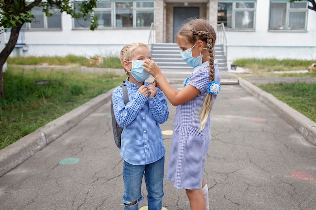 Back to school siblings with backpacks in medical masks stay near doors before first offline day