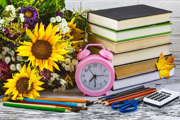 Back to school a stack of books a pink alarm clock stationery an apple autumn flowers