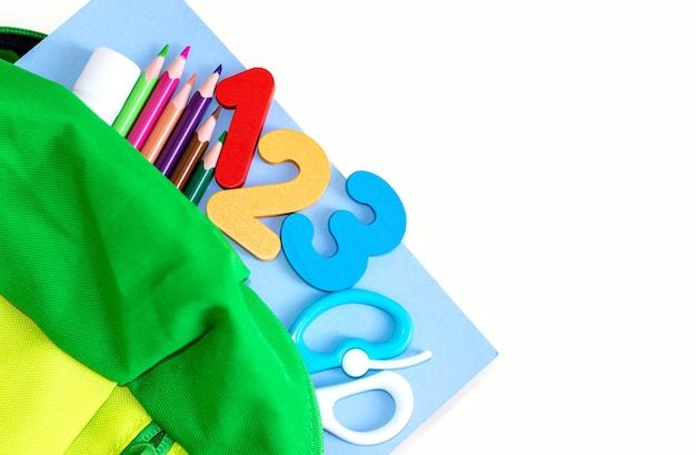 Photo back to school.supplies in green backpack for kids,pencils,blue paper,glue,scissors and colorful