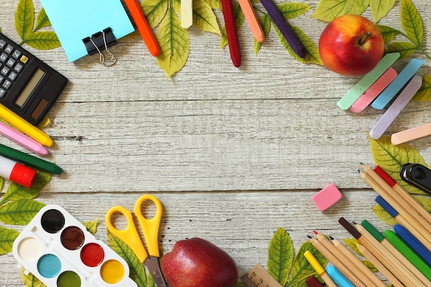 Ritorno a scuola tavolo con foglie autunnali e diversi articoli di cancelleria per la scuola vista dall'alto