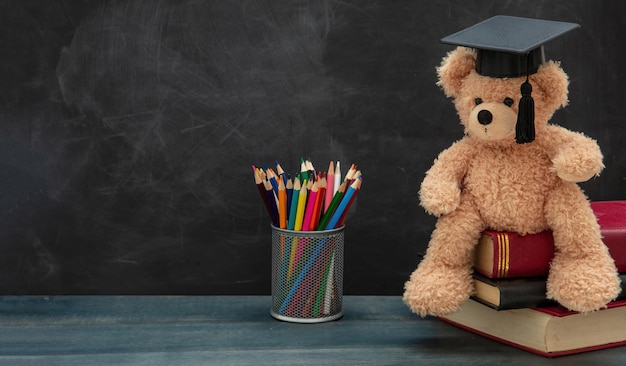 Back to school teddy bear with graduation cap books and pencils\
on desk