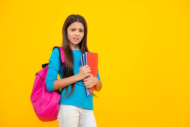 Back to school teenager schoolgirl hold book and copybook ready\
to learn school children on isolated yellow studio background angry\
face upset emotions of teenager girl