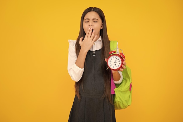 Back to school teenager schoolgirl with bag hold clock alarm time to learn school children on isolated yellow background tired and bored teenager girl