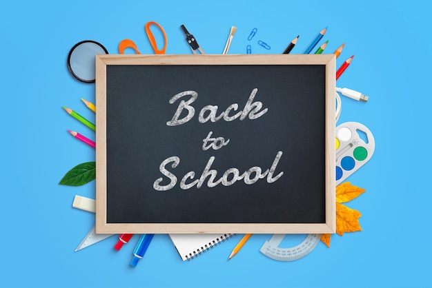 Back to school text on chalkboard surrounded by school supplies Top view flat lay composition on blue work desk