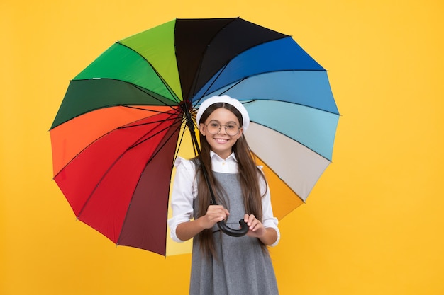 Back to school. tween with vivid rain protection. happy school girl in glasses. cheerful teen child under colorful parasol. kid in beret with rainbow umbrella. autumn season. rainy weather forecast.